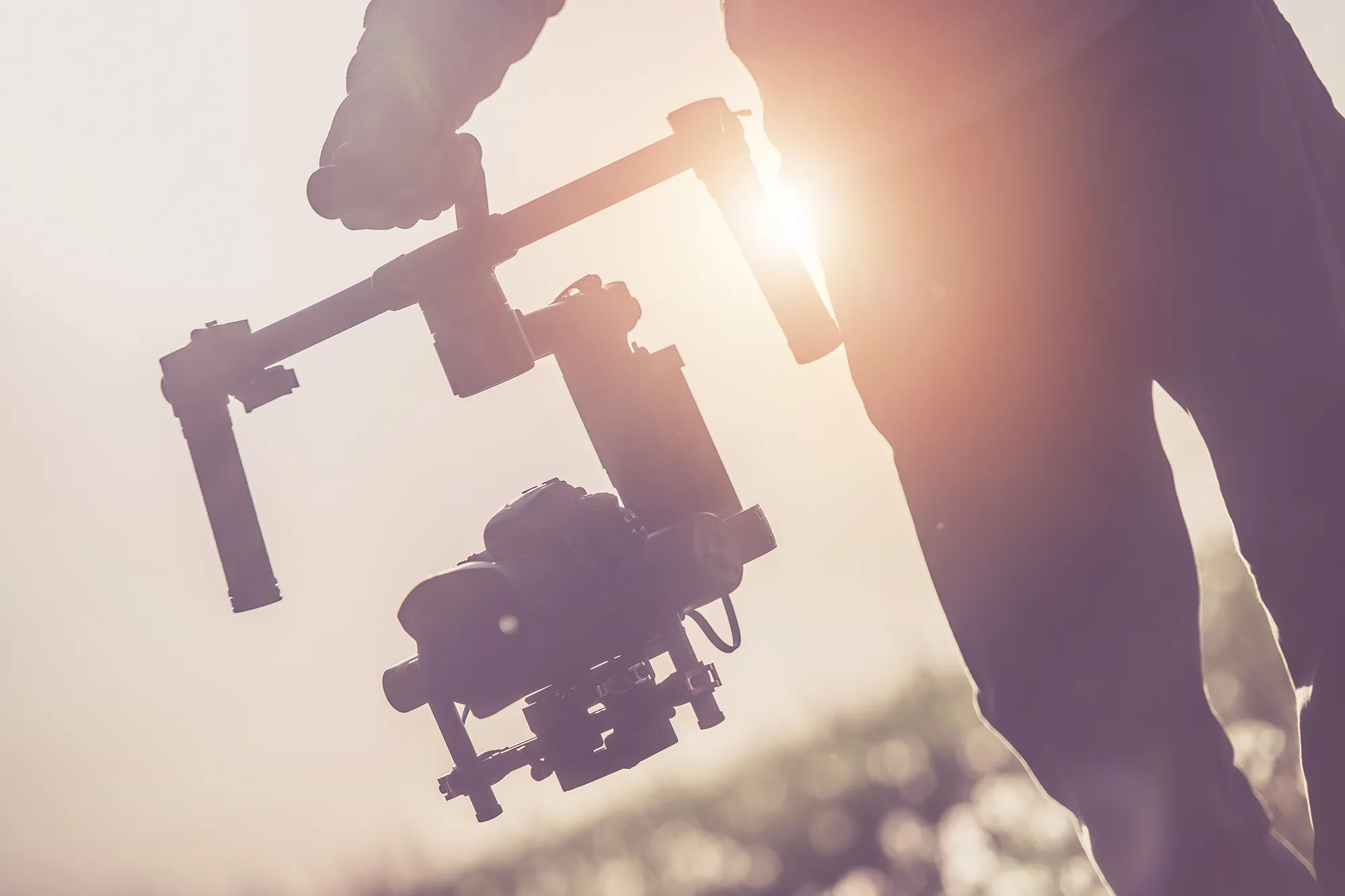 Person holding a gimbal video stabilizer with the sun causing a lens flare in the background